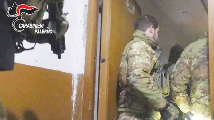 Italy Two uniformed officers of the Carabinieri wearing jackets with a camouflage print stand in a doorway while a colleague behind them holds a gun. Italy's military police launched the operation in the early hours of Tuesday against the Mafia. CARABINIERI PALERMO