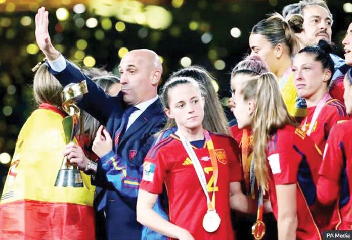 Spain-1 Luis Rubiales holds the Women’s Football World Cup Trophy on the day of the final. He is surrounded by the players who are all looking away from him while he waves to the crowd. Prosecutors are calling for Rubiales to be jailed for sexual assault. PA Media