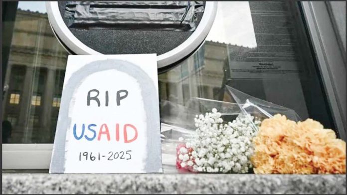 A sign placed reading “RIP USAID 1961-2925” and flowers are placed beneath the covered seal of the US Agency for International Development headquarters in Washington, DC. AFP