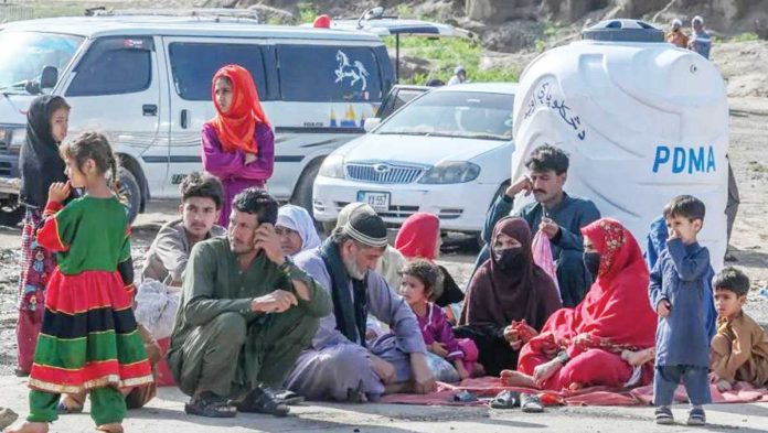 Pakistan-1 A scene at the Torkham crossing showing men, women and children sitting on the floor. There are several vehicles in the background. GETTY IMAGES