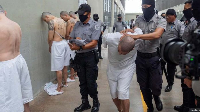 US Several prisoners are lined up against the wall as masked guards move a shackled prisoner in Tecoluca, El Salvador last week during a visit by US Homeland Security Secretary Kristi Noem. REUTERS