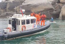 Taiwanese coast guard personnel apprehend a suspect who appears to be kneeling on a small floating platform. The vessels are by large rocks.TAIWAN COAST GUARD ADMINISTRATION