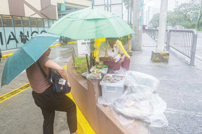 wage_hikes_resized President Ferdinand "Bongbong" Marcos' economic team estimates that a P200-increase in wages could raise inflation by around 2 percentage points, and could hurt the poor as well as small businesses. Photo shows an elderly street vendor selling native delicacies under pouring rain in Katipunan Avenue, Quezon City on June 11, 2025. PNA PHOTO BY ROBERT OSWALD P. ALFILER