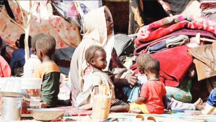 A woman and five young children sit amid piles of fabric, clothing and matting, under makeshift tents that have been propped up by small trees in Sudan where 12 million people have been displaced by conflict. REUTERS