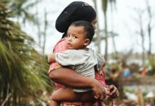 A Rohingya woman carries her baby next to her destroyed house at Basara refugee camp in Sittwe, Myanmar. Communal fighting and war have displaced some hundreds of thousands of Rohingya in Rakhine State, Myanmar. GETTY IMAGES