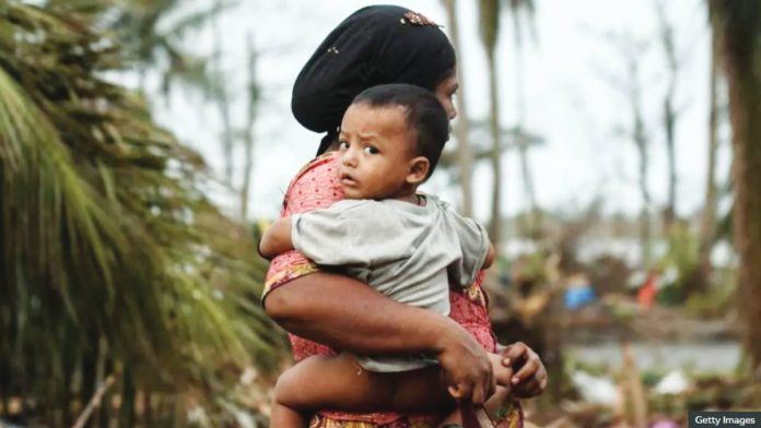 Myanmar A Rohingya woman carries her baby next to her destroyed house at Basara refugee camp in Sittwe, Myanmar. Communal fighting and war have displaced some hundreds of thousands of Rohingya in Rakhine State, Myanmar. GETTY IMAGES
