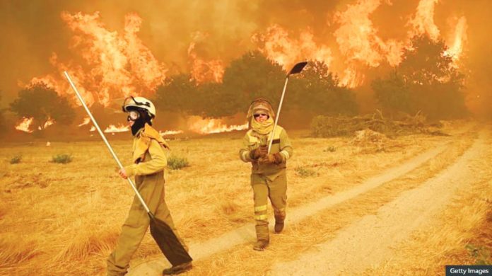 Spain Firefighters tackle a raging inferno in a Spanish woodland scene. The grass around them is dry and parched, and the trees in the background are completely aflame. GETTY IMAGES