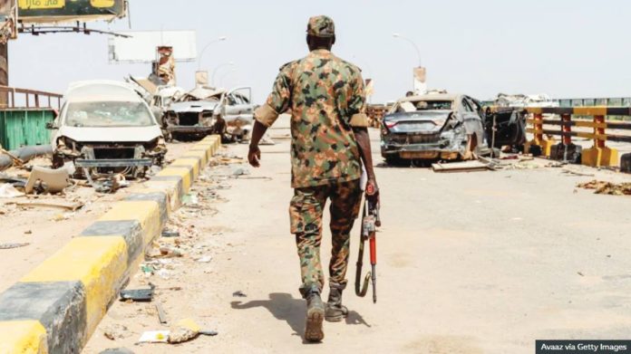 Sudan A lone soldier walks across a bridge in Sudan. Bombed-out cars and rubble can be seen on the bridge. GETTY IMAGES