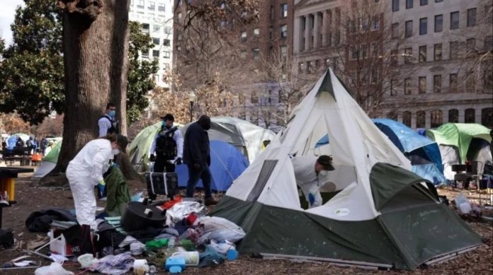 A tent encampment of homeless people in a public park is being removed from downtown Washington DC by workers in hazmat suits and face masks. Rubbish is seen strewn outside of one white and green tent. GETTY IMAGES