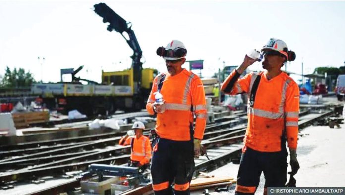 WHO.JPG_resized Laborers wearing hi-viz orange tops drink water to cool down as they work on a construction site of tramway lines along the Garonne river in France. The World Health Organization has said that climate change will leave construction workers especially vulnerable to heat stress. AFP
