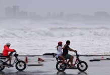 Rising seas threaten 1.5M Australians Three people ride two bikes in the coast in Australia with waves crashing in the background. Australians are already living with the consequences of climate change. EPA