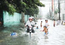 A FLOOD OF INCONVENIENCE. A motorcycle negotiates a flooded street in Makati City while children, unmindful of health dangers, play. Inclement weather usually brings rains that submerge in floods the streets of Metro Manila. PNA