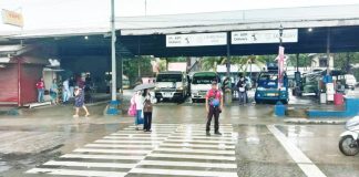 Intermittent rains forced the suspension of in-person classes in Iloilo City schools on Monday, Sept. 22, 2025. Photo shows a traffic enforcer assisting two students crossing the pedestrian lane in front of a transport terminal in Barangay Ungka, Jaro district during rainy Monday morning. ICTTMO PHOTO