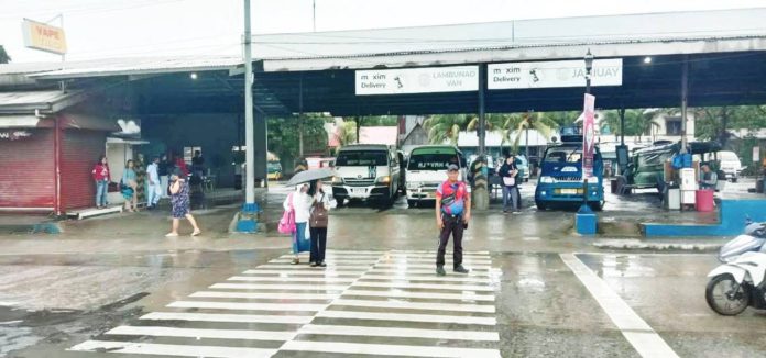 iloilo_city_pic_resized Intermittent rains forced the suspension of in-person classes in Iloilo City schools on Monday, Sept. 22, 2025. Photo shows a traffic enforcer assisting two students crossing the pedestrian lane in front of a transport terminal in Barangay Ungka, Jaro district during rainy Monday morning. ICTTMO PHOTO