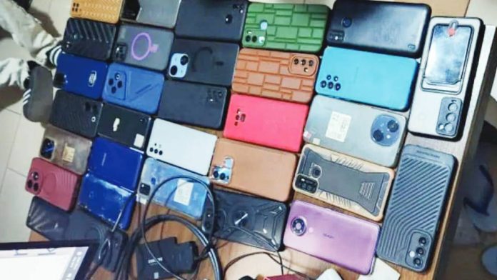 A closeup of different brands of seized phones and chargers placed on a table. These were used to carry out sextortion and romance scams in the African continent, according to Interpol. INTERPOL