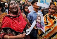 Two tearful women in the foreground hold on to photographs of their loved ones printed on paper. A larger crowd has gathered behind them, many of them also clutching onto photographs of their relatives still missing after a fire blazed through a garment factory in Bangladesh. GETTY IMAGES