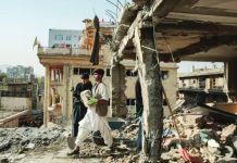 Two young men, one in all black holding a spade and another in white carrying a brick, stand amid the rubble of a destroyed building in Kabul. EPA