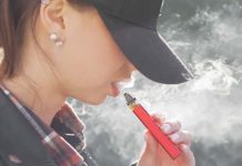 A young woman draws on a vape or e-cigarette while the vapor blows around her mouth and face. GETTY IMAGES