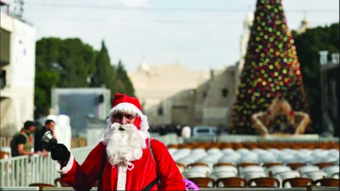 Bethlehem_resized_compressed A man dressed as Santa Claus stands in Manger Square ahead of the lighting of the Christmas tree in the West Bank city of Bethlehem. EPA