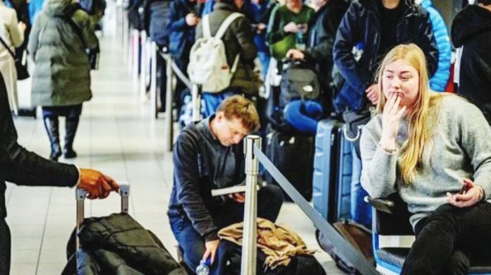 Europe Travellers queue with their luggage at Schiphol Airport. One woman is sitting with her phone in her hand, while a man behind her is kneeling next to his bag while reading a book. Hundreds of people were stranded at Amsterdam airport. GETTY IMAGES