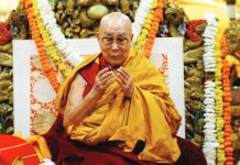 The Dalai Lama sits on a throne wreathed in floral arrangements. REUTERS