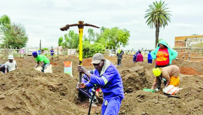 South_Africa_resized_compressed A man holds a pickaxe aloft in an area used recently as a cattle enclosure in South Africa. Other people can be seen digging for gold behind him. EPA/SHUTTERSTOCK