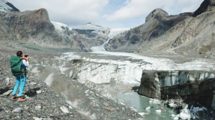 A scientist takes a photo as part of an annual monitoring project of Austrian glaciers administered by the Austrian Alpine Association. In the background are glacier slopes down the rocky mountainside, while in the foreground chunks of ice are in a stream. GETTY IMAGES