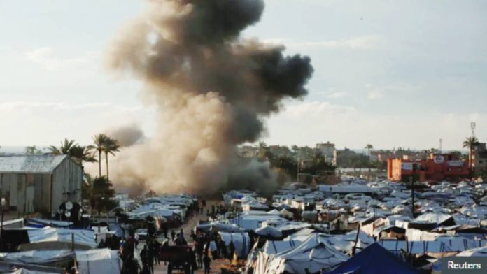 Smoke can be seen rising behind a tent camp following an Israeli strike in the central Gaza Strip. REUTERS