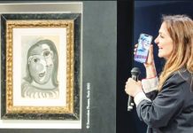 A blue painting by Picasso, in his trademark cubist style, is seen framed on the wall beside a woman holding a microphone up to her mobile phone, which shows a video call with Ari Hodara who was drawn at random as winner of the painting from more than 120,000 ticket-buyers worldwide. EPA
