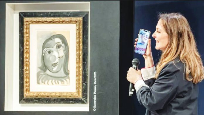 A blue painting by Picasso, in his trademark cubist style, is seen framed on the wall beside a woman holding a microphone up to her mobile phone, which shows a video call with Ari Hodara who was drawn at random as winner of the painting from more than 120,000 ticket-buyers worldwide. EPA