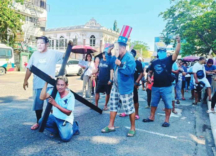 Kalbaryo sang Pumuluyo BIBLICAL-LEVEL SUFFERING. A jeepney driver bears a wooden cross along a busy Iloilo City street, dramatizing the crushing burden of soaring fuel prices as protesters liken the daily struggle of commuters and drivers to Christ’s suffering at Calvary. BAYAN-PANAY PHOTO