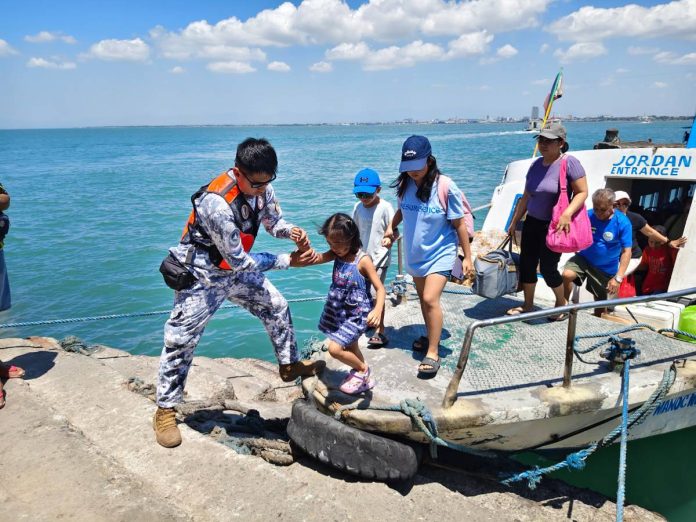 ime coastguard A Philippine Coast Guard personnel assists a young passenger as pilgrims and travelers disembark at a port in Guimaras during the Holy Week rush, part of intensified safety operations across Western Visayas. PHOTO FROM PCG- GUIMARAS STATION