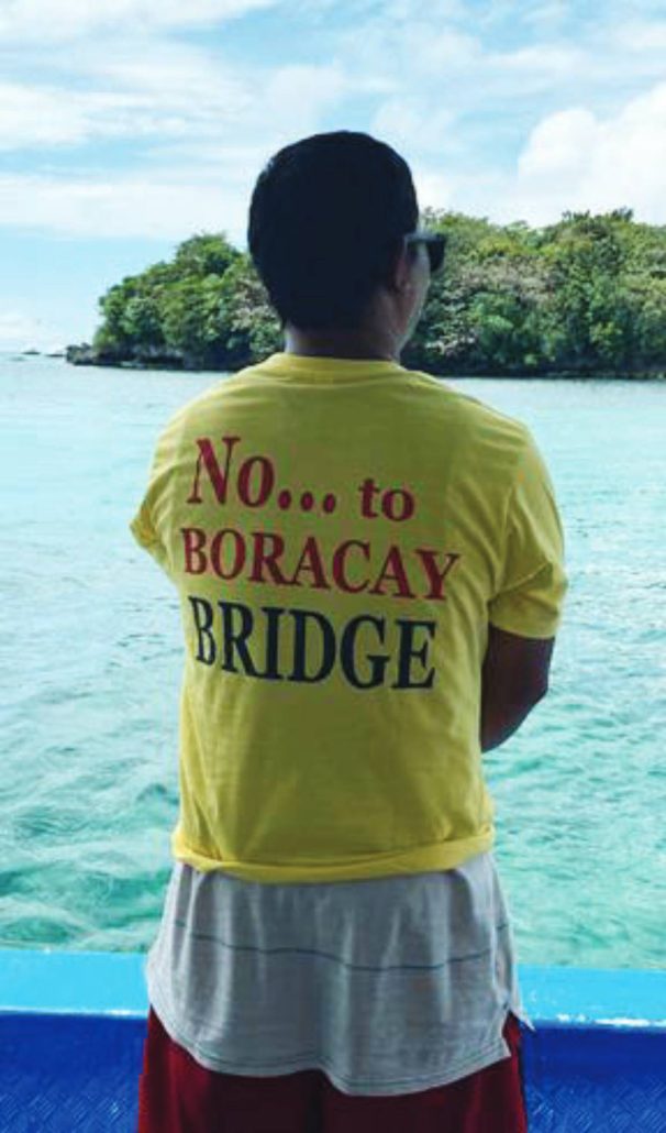 Facing the waters that sustain him, a boatman wears his opposition on his back — a simple statement carrying the weight of jobs, families, and a community’s future.