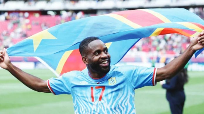 Congolese football player Cédric Bakambu celebrates with the national flag on a football pitch. The Democratic Republic of Congo has qualified for the FIFA World Cup for the first time since 1974. GETTY IMAGES