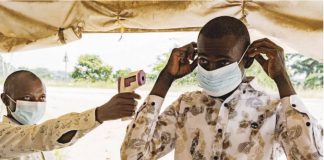 A Congolese man wearing a mask holds up a contactless thermometer to a man who is putting on a mask for protection. AFP VIA GETTY IMAGES