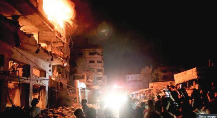 People look on as fire burns in a building in central Gaza City. GETTY IMAGES
