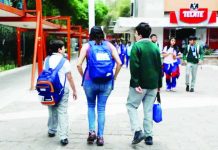 A mother picks up her children from an elementary school in Mexico City. She is flanked by a smaller boy, who is carrying a backpack, and a bigger boy, who is carrying a bag in his hand. Other children are walking towards them. SASHENKA GUTIERREZ/EPA/SHUTTERSTO