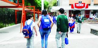 A mother picks up her children from an elementary school in Mexico City. She is flanked by a smaller boy, who is carrying a backpack, and a bigger boy, who is carrying a bag in his hand. Other children are walking towards them. SASHENKA GUTIERREZ/EPA/SHUTTERSTO