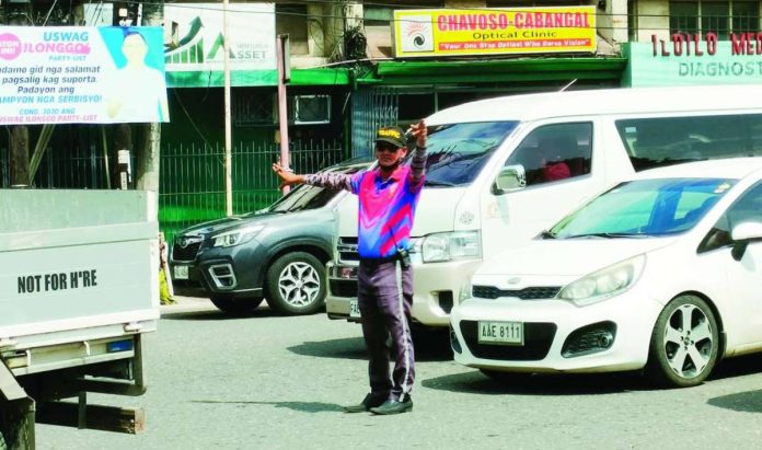 front_pic2_compressed_resized A traffic aide directs vehicles along Bonifacio Drive in Iloilo City’s City Proper district. Traffic management in the city is expected to get a boost as the Traffic and Transportation Management Office pushes to deputize barangay officials and tanods to strengthen community-based traffic enforcement and anti-illegal parking efforts. AJ PALCULLO/PN