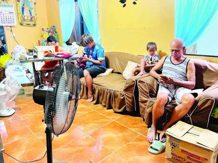 front_pic_compressed_resized A family in Barotac Nuevo, Iloilo utilizes two electric fans inside their home on Tuesday, May 19, seeking relief as summer temperatures continue to soar. As household appliance use spikes due to the intense summer heat, power distributors across Western Visayas report that peak-hour demand is putting a heavy strain on power reserves, prompting calls for strict energy conservation. PN PHOTO