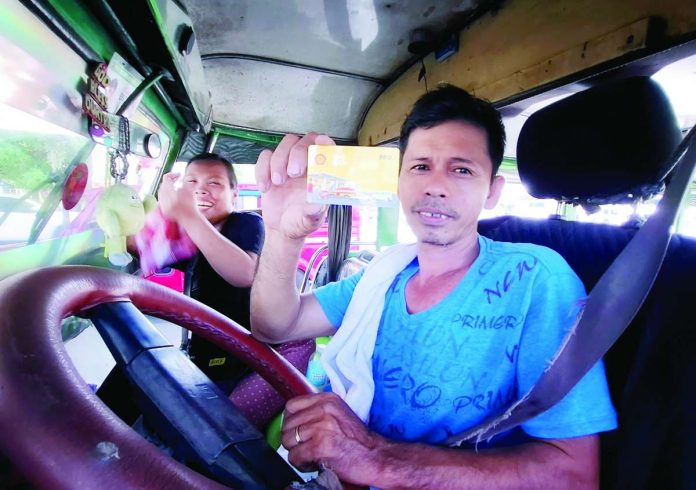 A public utility jeepney driver shows his diesel fuel discount card as he stops to refuel at a gas station in Quimpo Boulevard in Davao City. His wife, who serves as his conductor, is all smiles about the P10-per-liter discount they received through the government fuel subsidy program. She says life is hard so she has to work, too. PNA