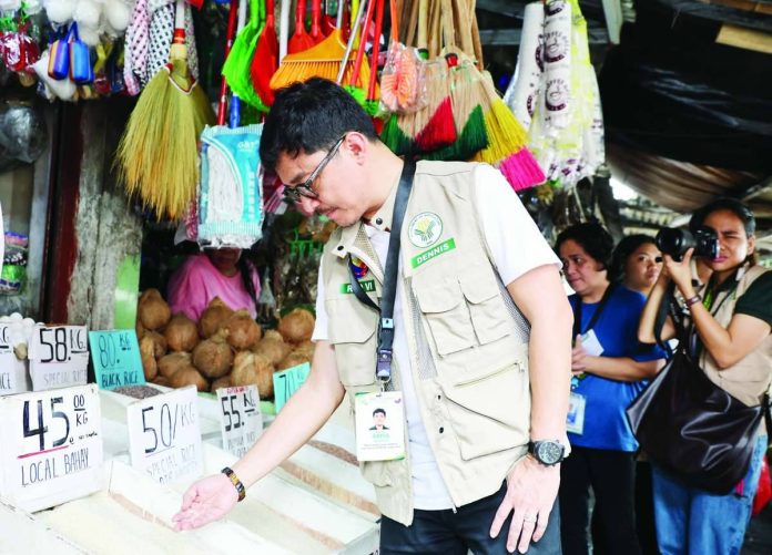 Regional Executive Director Dennis Arpia of the Department of Agriculture in Western Visayas checks rice stocks and prevailing market prices during an inspection at a public market in Iloilo City on June 1, 2026. The monitoring aims to ensure that retailers and traders comply with the P50-per-kilogam price cap on five-percent broken imported rice.