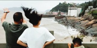 A man, woman and child stand behind a cemented barrier, looking at muddy waters in a coastal region. Typhoon Bavi has passed through the coastal village of Diaocaocun in Zhejiang province, China. REUTERS