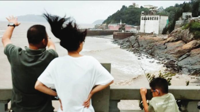 China A man, woman and child stand behind a cemented barrier, looking at muddy waters in a coastal region. Typhoon Bavi has passed through the coastal village of Diaocaocun in Zhejiang province, China. REUTERS