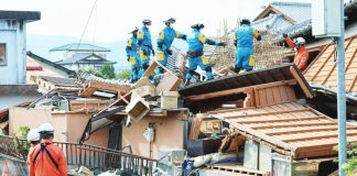 Rescue workers in overalls stand on top of a collapsed house at Kumamoto prefecture on Kyushu Island, Japan. A strong earthquake caused widespread damage to houses and power lines across Kumamoto. JIJI PRESS / AFP VIA GETTY IMAGES