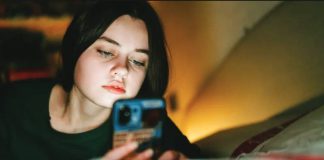 A teenage girl looks at her phone at nighttime in low lighting with the glow of a lamp. Older teenagers in the United Kingdom will face an overnight social media curfew. GETTY IMAGES