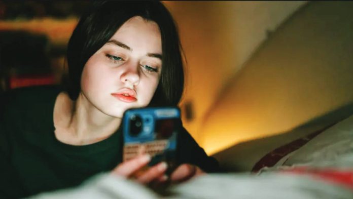 UK A teenage girl looks at her phone at nighttime in low lighting with the glow of a lamp. Older teenagers in the United Kingdom will face an overnight social media curfew. GETTY IMAGES