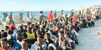 Migrants sit on the ground in rows at the beach with the sea behind them in Ceuta, Spain waiting for aid. GETTY IMAGES