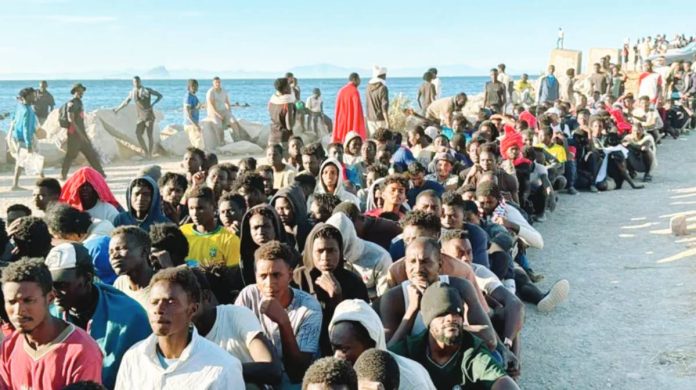 EU Migrants sit on the ground in rows at the beach with the sea behind them in Ceuta, Spain waiting for aid. GETTY IMAGES