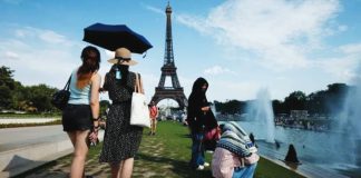 Women shelter from the heat under a black umbrella at the Trocadero Fountain by the Eiffel Tower, in Paris, France. Other people are seated next to the river. EPA